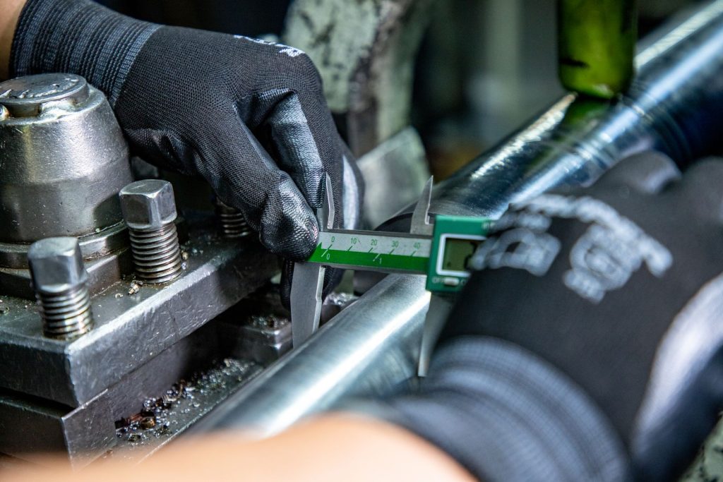 Gloved hands using a caliper to check the diameter of a metal shaft