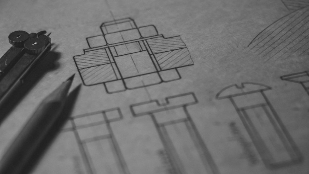 Pencil and compass beside a mechanical assembly sketch